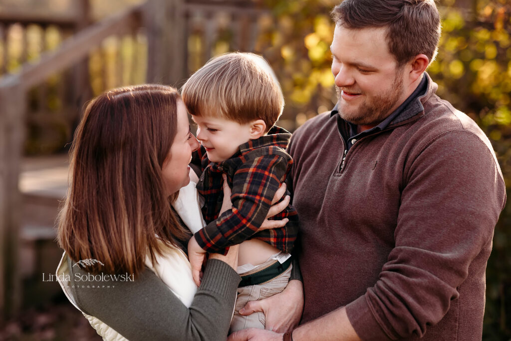 parents hugging their little boy at the park, Beautiful Family photos in the fall with CT Shoreline photographer