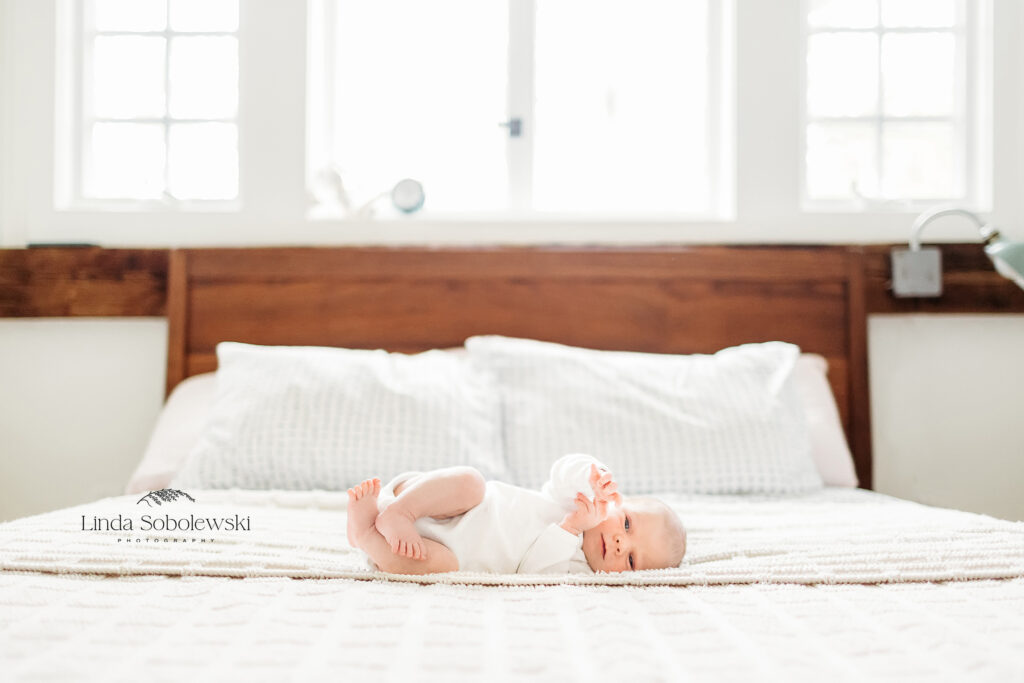 baby laying in bed with white sheets, CT shoreline photographer