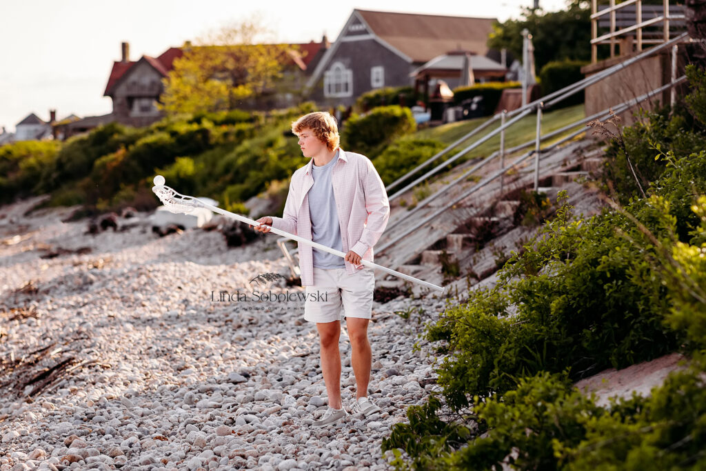 teenage boy holding lacrosse stick for his senior photo session, CT shoreline photographer