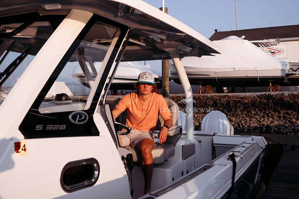 boy in orange shirt and white hat sitting in his boat, CT high school senior boy photo session