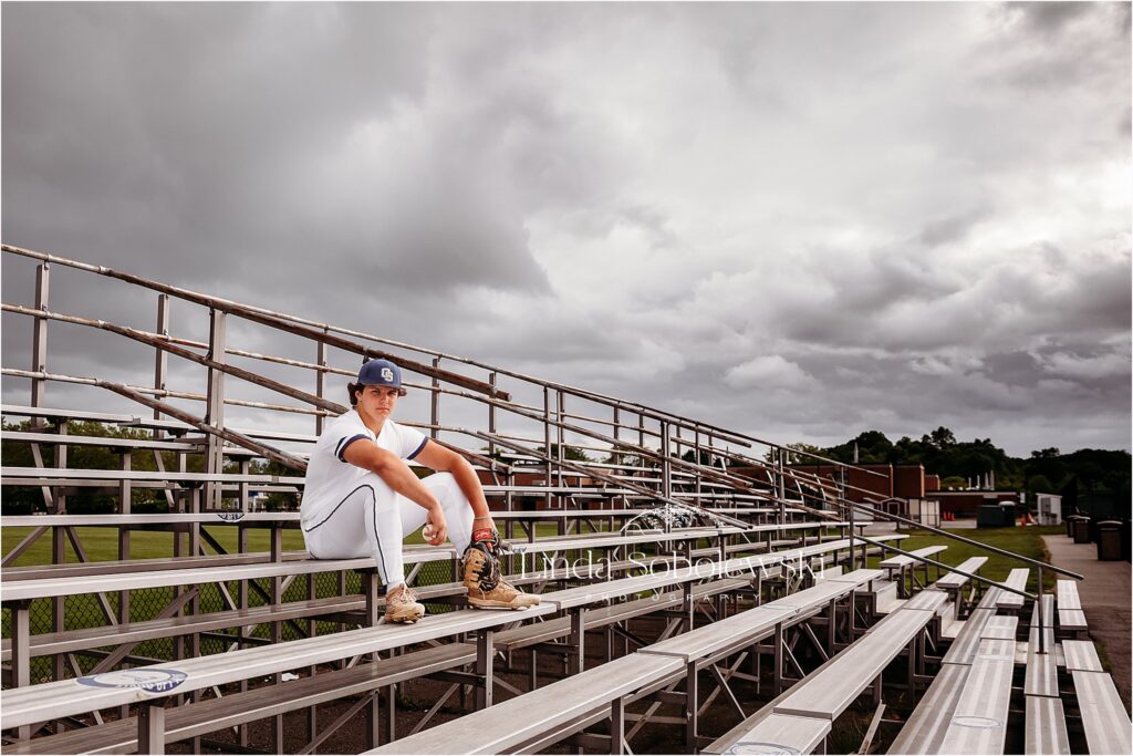 teenage boy in baseball uniform sitting in the metal stands, Old Saybrook CT senior photographer