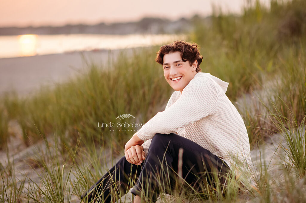 teenage boy with black hair sitting at the beach in the grass, CT Shoreline best photographer