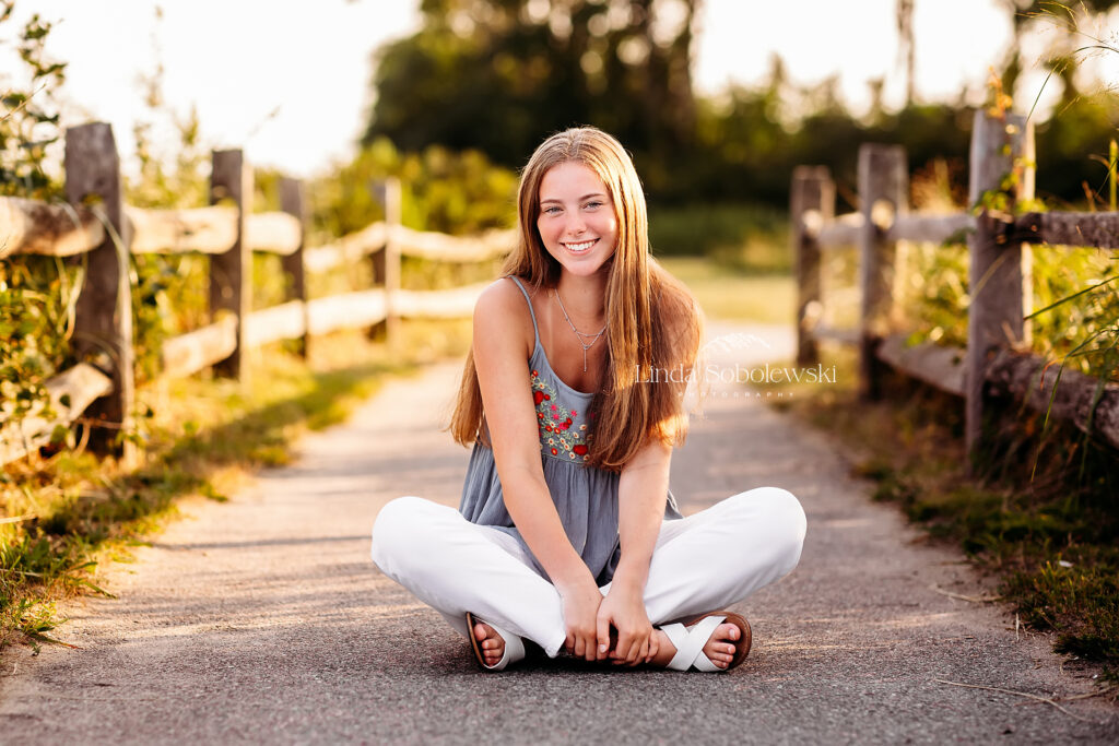 teenage girl in blue top and white jeans sitting on the ground, CT Best senior photographer