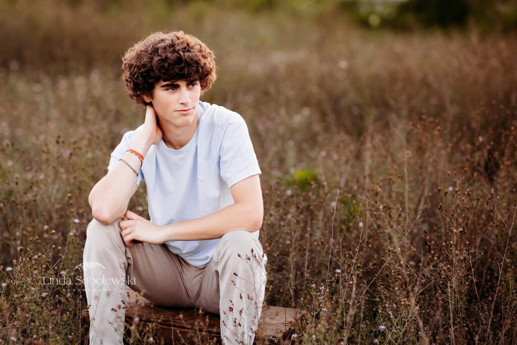teenage boy in a white shirt sitting in a field, Old Saybrook CT senior photographer