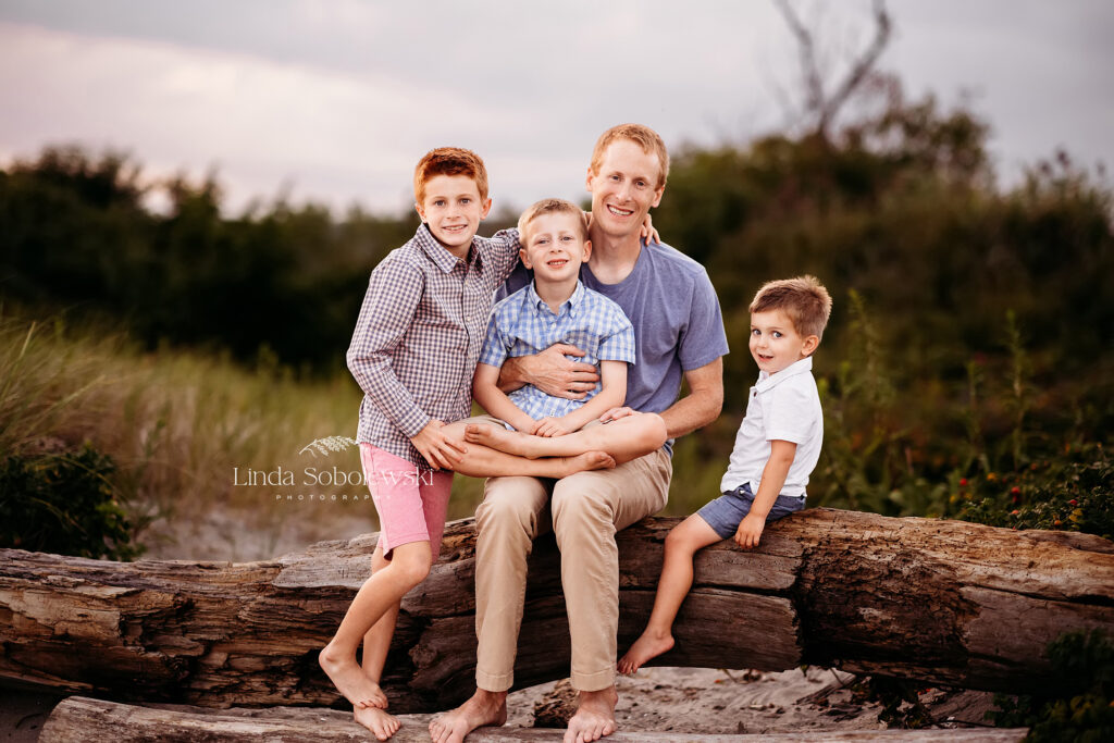 father and his three boys sitting together on a log at the beach, CT Senior and family photographer