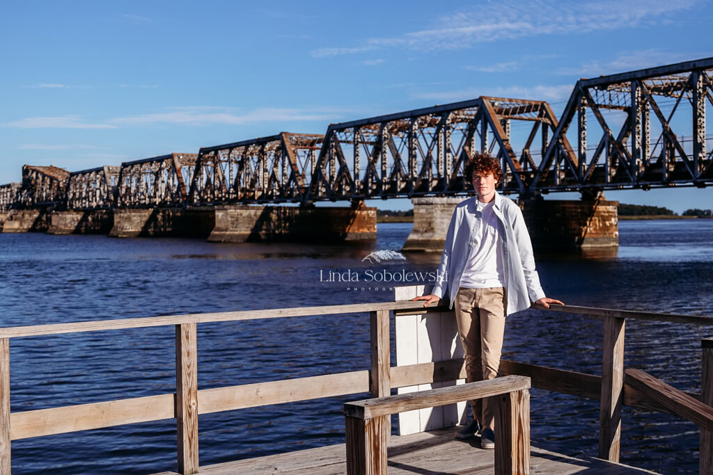 teenage boy leaning against a fence with a bridge behind him, Best Senior Photographers in CT