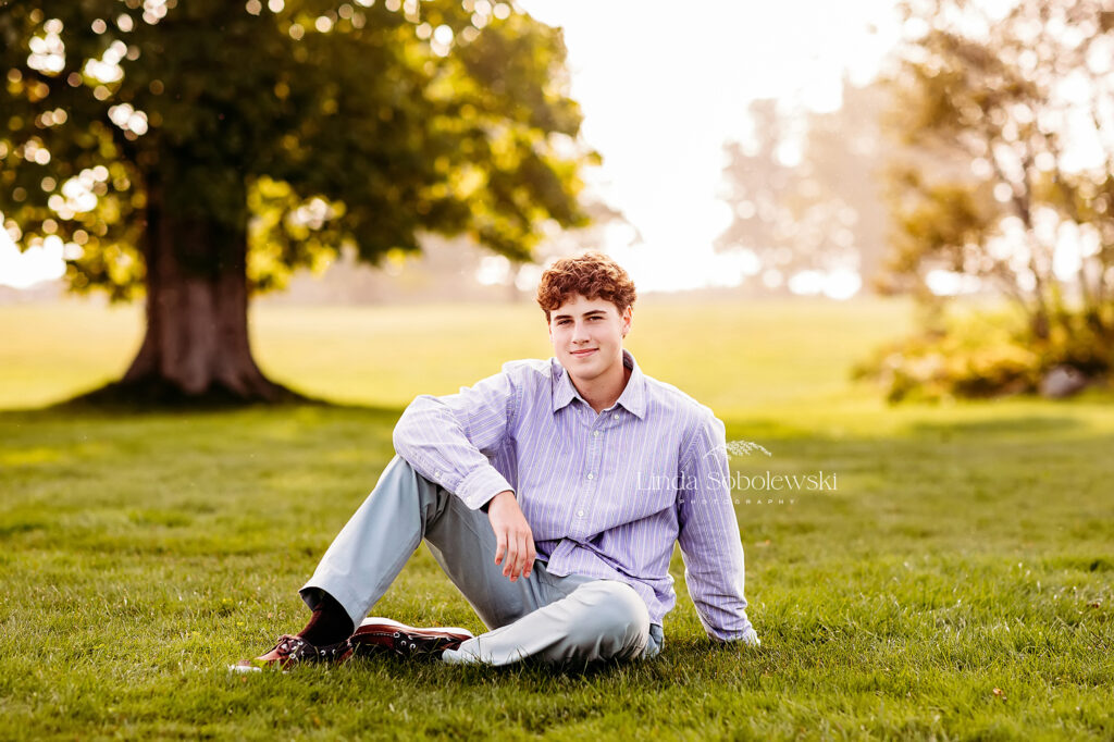 teenage boy sitting in the grass for his senior photo session at Harkness Memorial Park in Waterford, CT