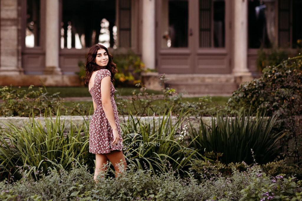 girl in floral dress standing next to a mansion, Senior photos taken at harkness Park