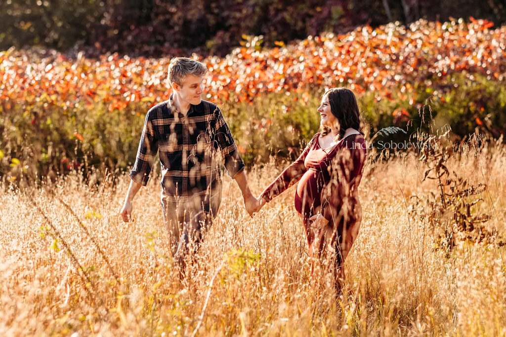 pregnant woman in red dress with husband in a field for a maternity photoshoot in CT