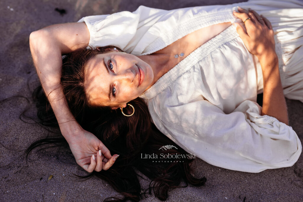 teenage girl in white dress laying in the sand, CT Best senior photographer