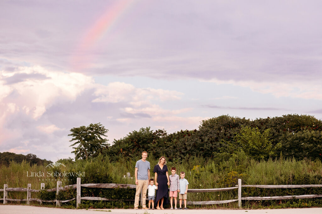 family of four standing against a fence with a rainbow in the skies, 2023 Session Superlatives blog post for CT photographer
