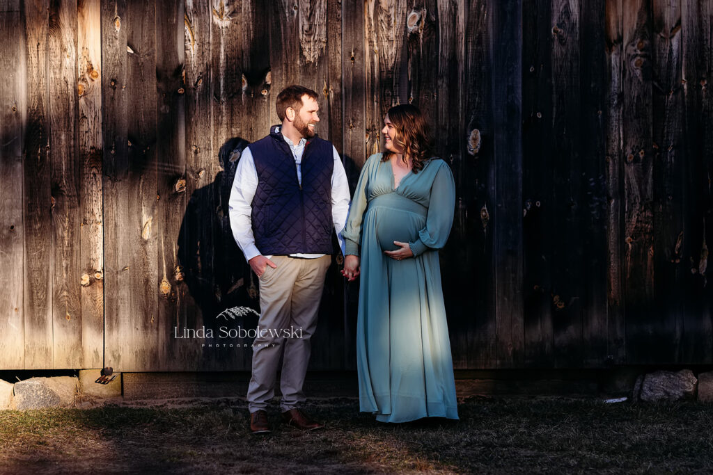 pregnant woman in green dress and her husband standing together in front of a barn, CT best maternity photographer