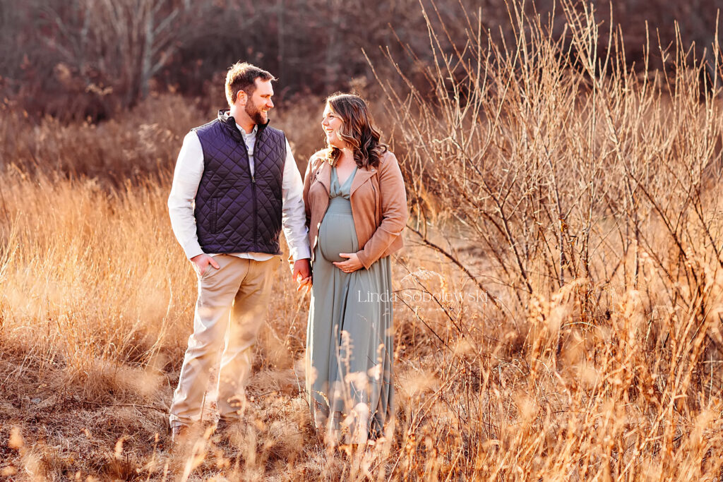 couple holding hands walking in a field, Winter maternity photos in CT
