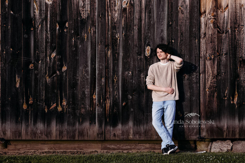 boy in tan sweater leaning against a barn, CT Shoreline senior photographer