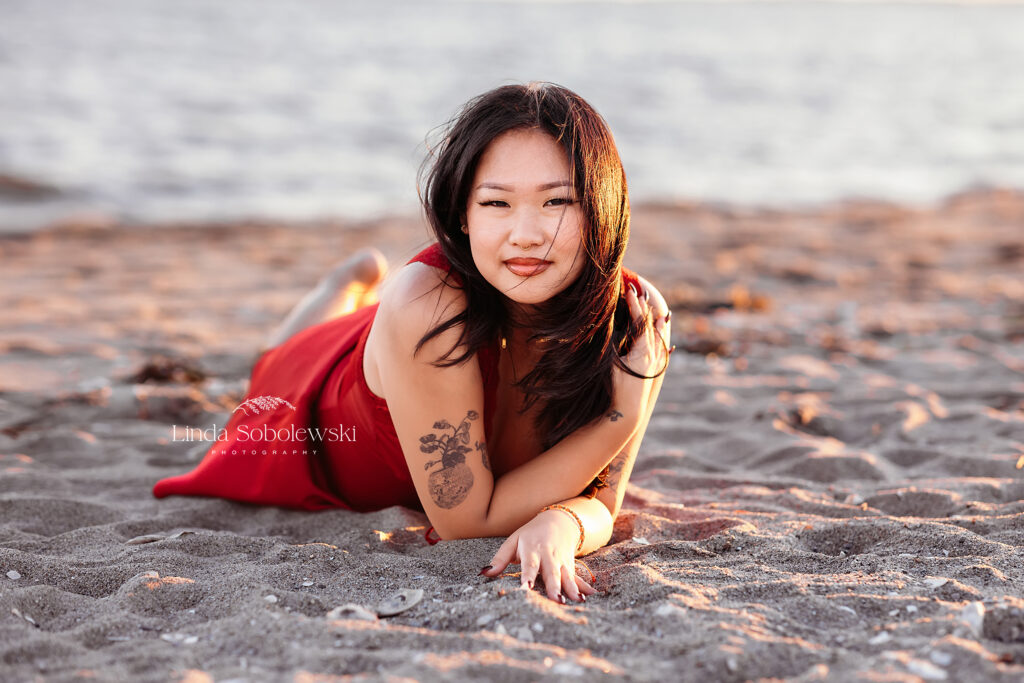 girl in black hair laying in the sand, Graduation Photos at the Beach, CT shoreline photograpehr