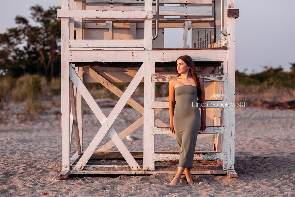 teenage girl in green dress leaning against a lifeguard chair, CT shoreline senior photographer