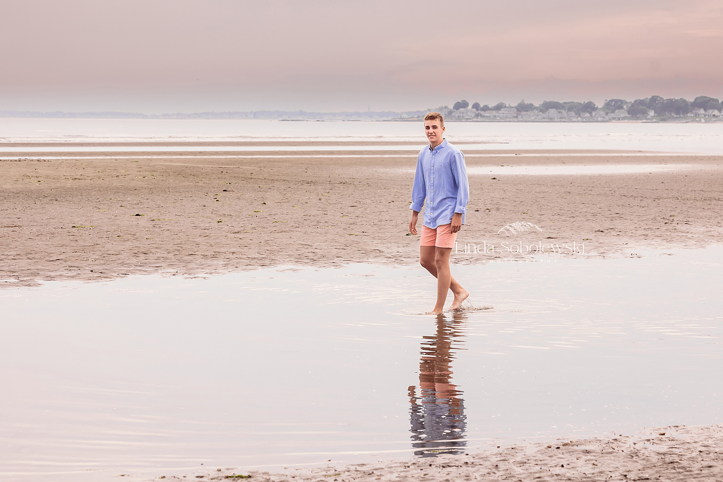 boy in blue shirt walking in the water, CT shoreline senior photographer