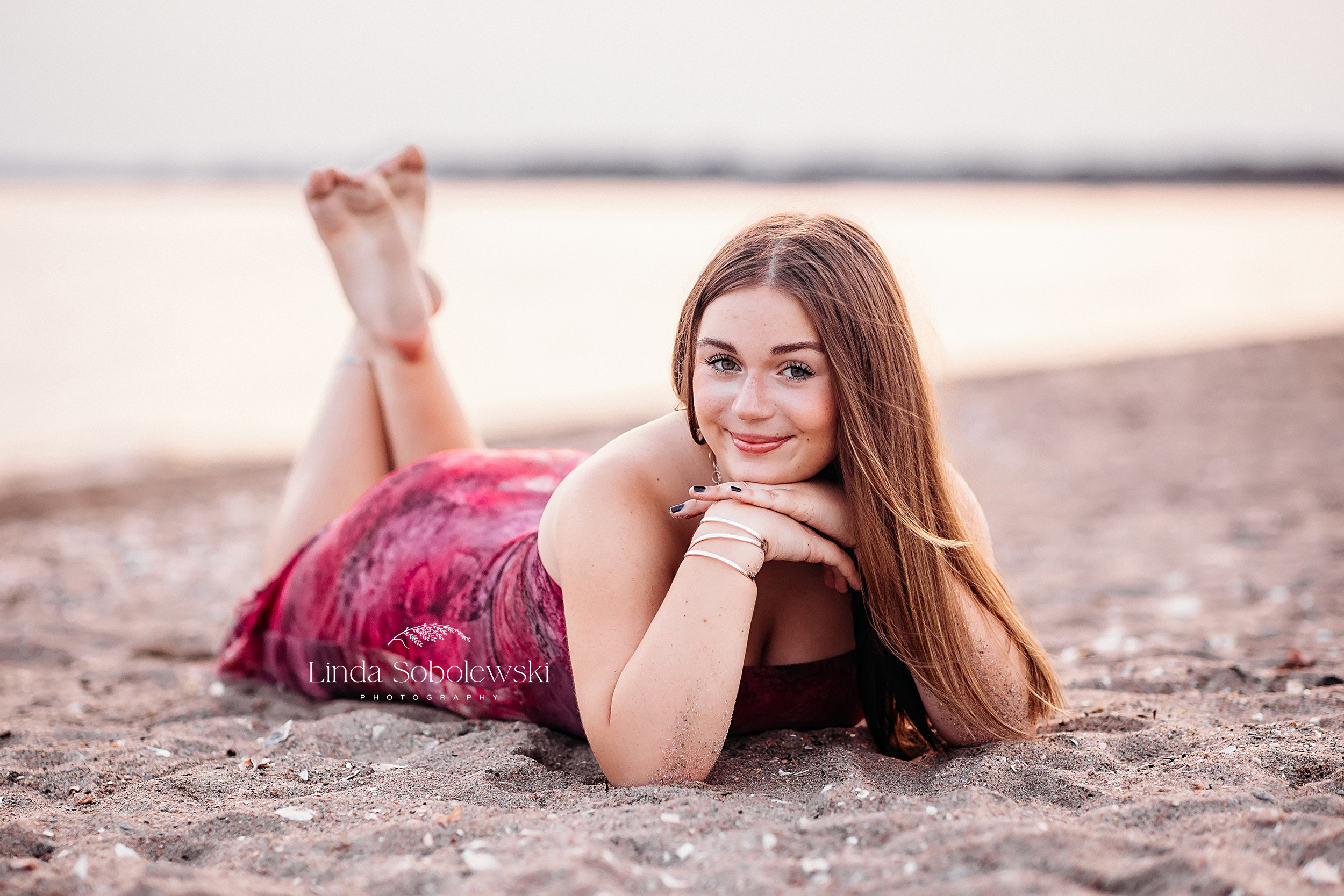 teenage girl with long hair laying on her stomach at the beach, CT best senior photographer