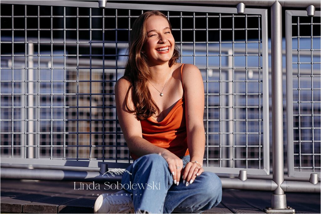 teenage girl in blue jeans laughing and leaning against a fence, Old Saybrook CT senior photographer