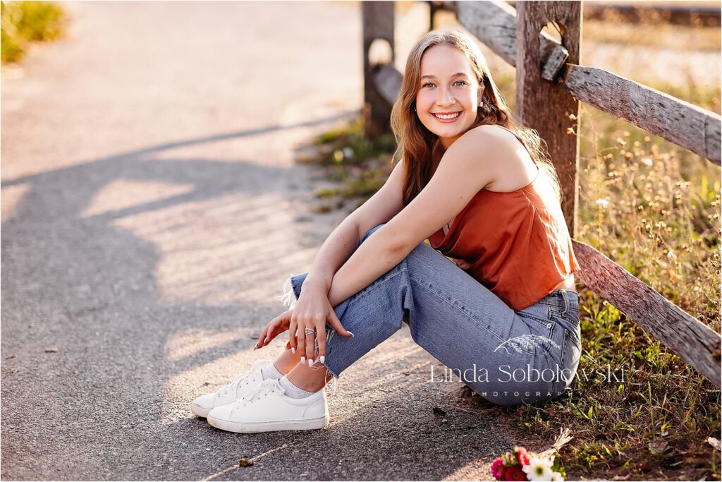 girl in blue jeans and white sneakers leaning against a fence, Senior photographer in CT