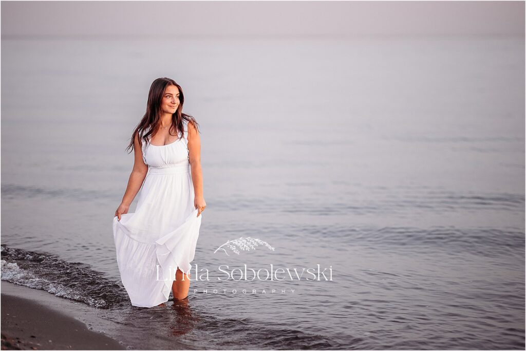 girl in long white dress walking along the water. CT shoreline senior photographer