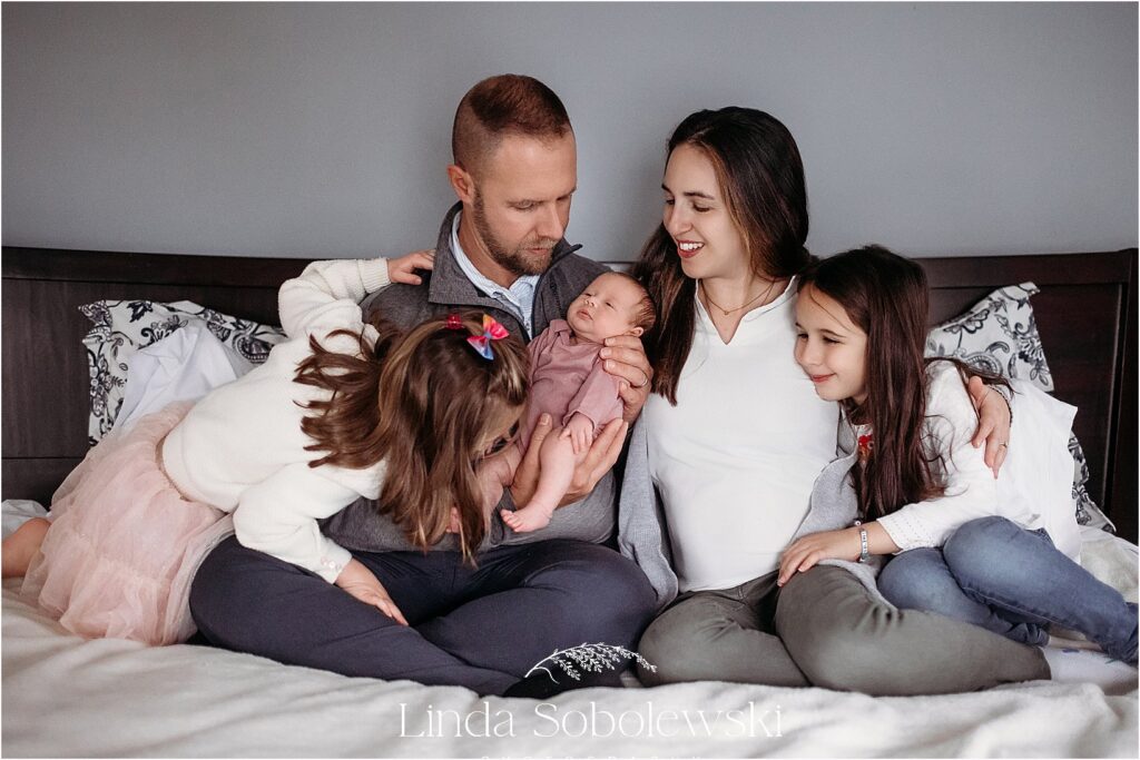 A loving family of five cuddles together on the bed, embracing their newest addition during a lifestyle newborn session.