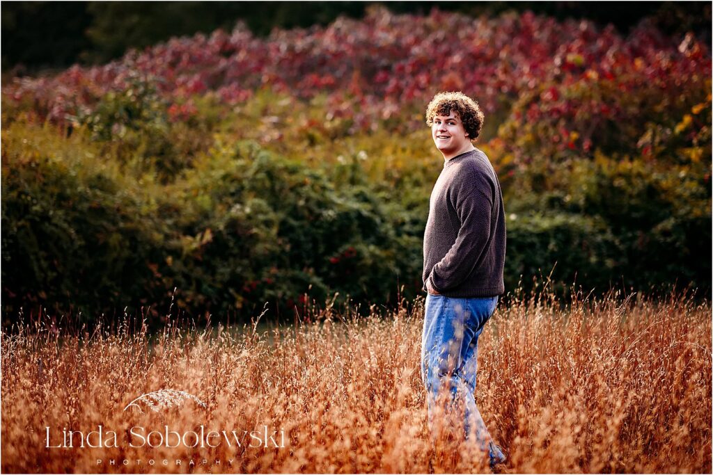 High school senior poses in a golden field during his senior photography session in Old Saybrook, CT, with rich autumn tones in the background.