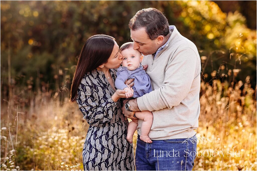 Family of three embracing in a golden autumn field during Fall Sessions in CT, with warm backlight and soft fall colors.