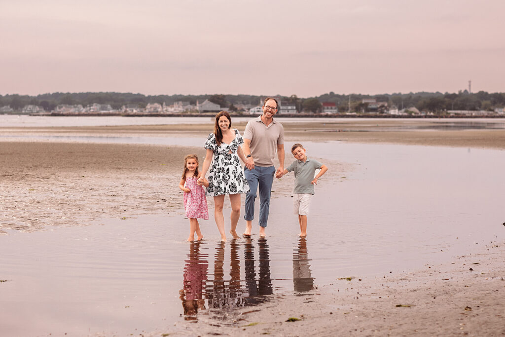 Family of four walking hand in hand through shallow water at the beach