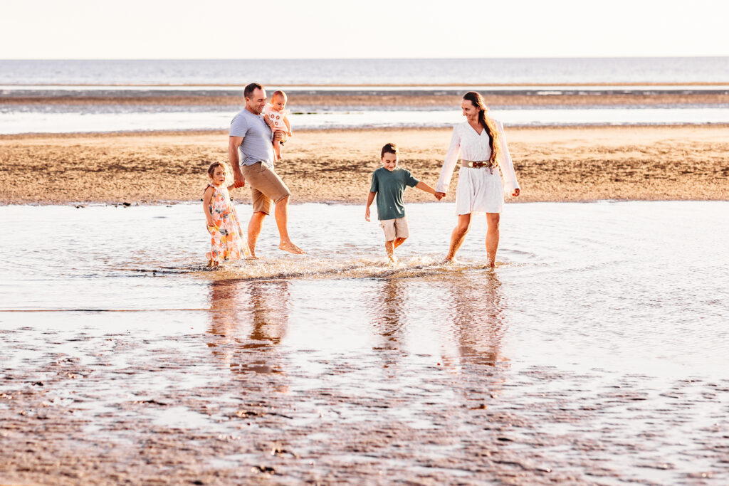 Young family holding hands while walking through glowing tide pools at golden hour, photographed by Linda Sobolewski in Old Saybrook, Connecticut.