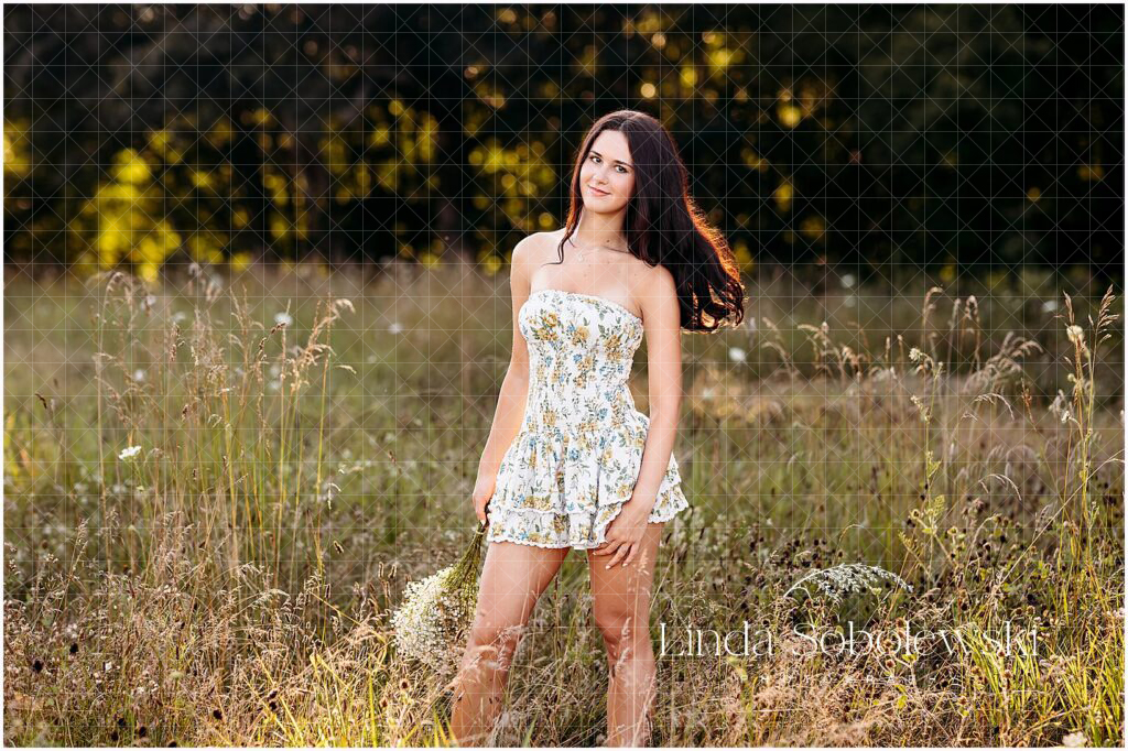 Smiling senior wearing a floral dress in a dreamy meadow, holding baby’s breath — Best CT Senior Photographer