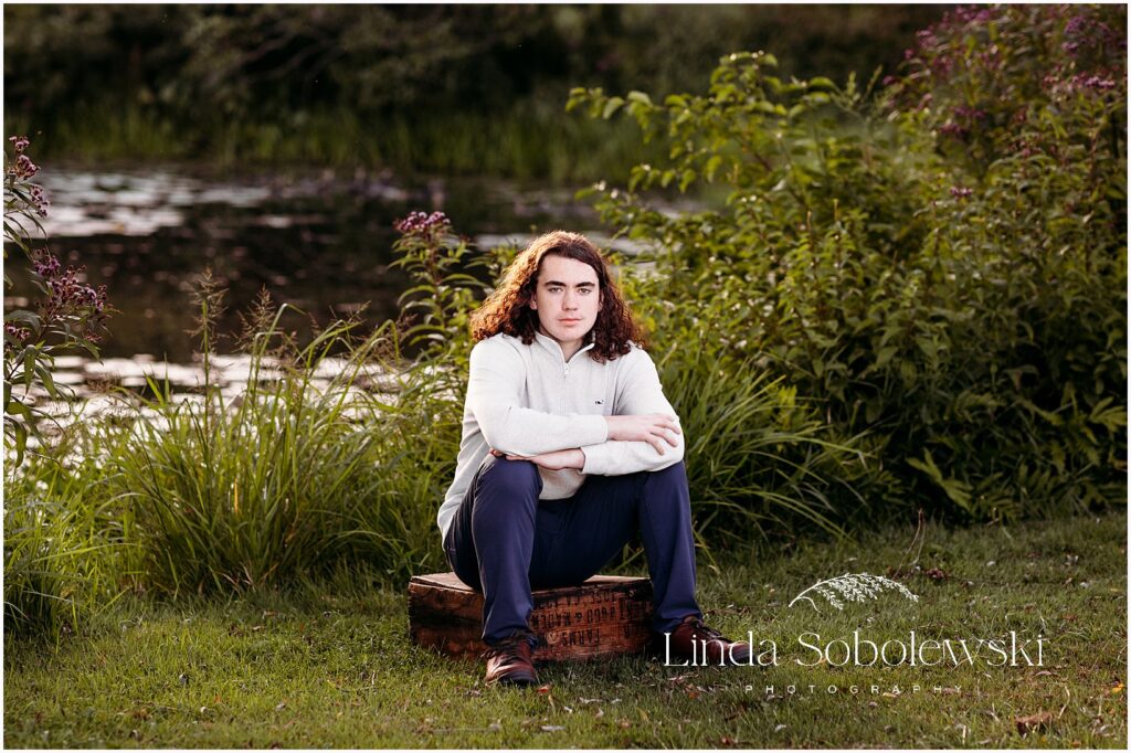 Teenage boy senior portrait sitting casually outdoors with relaxed posture and natural fall colors, Old Saybrook CT senior photographer