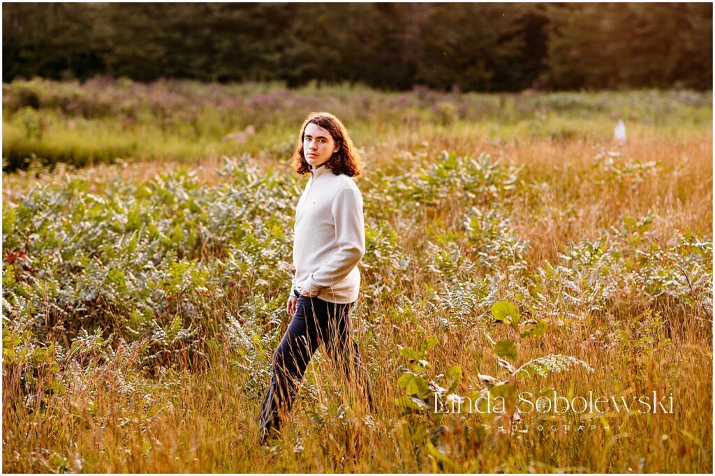 Senior boy portraits in Connecticut featuring a teenage boy standing in tall golden grass during late fall light, CT senior photographe