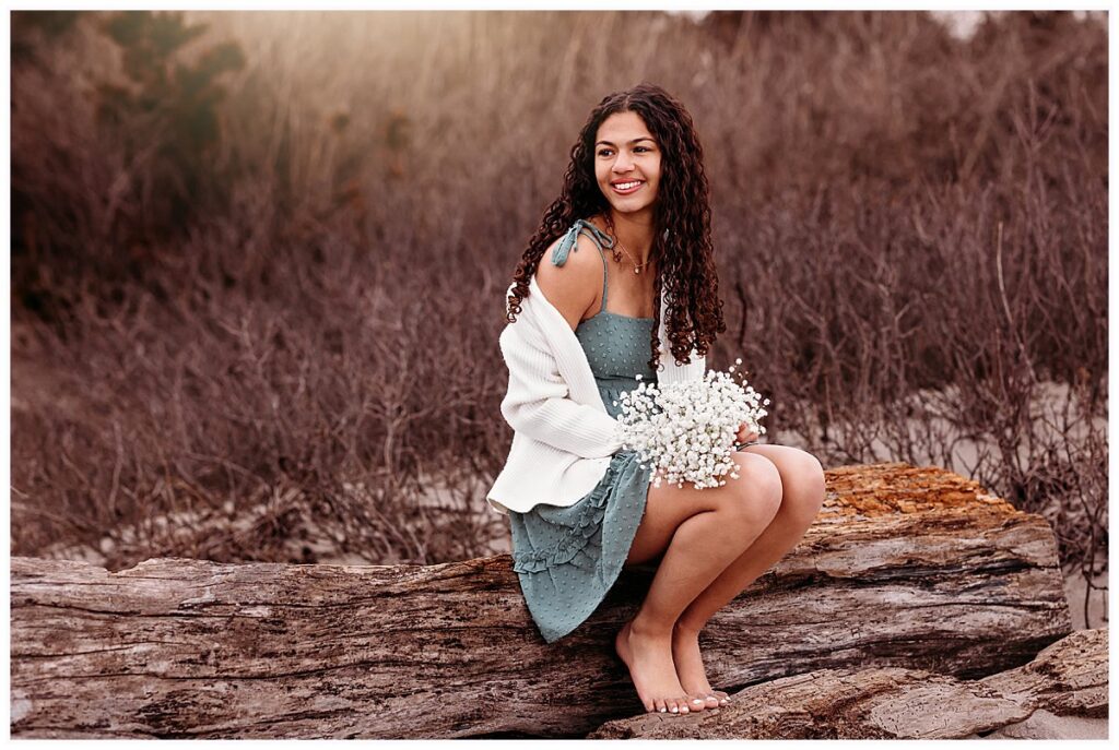 Senior girl in sage green dress sitting on driftwood at the beach, CT senior photographer