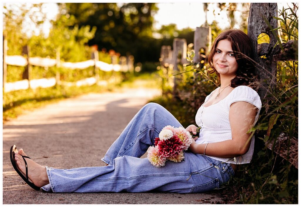Connecticut senior portraits of Lily holding colorful dahlias beside a rustic wooden fence.Madison, CT senior photographer